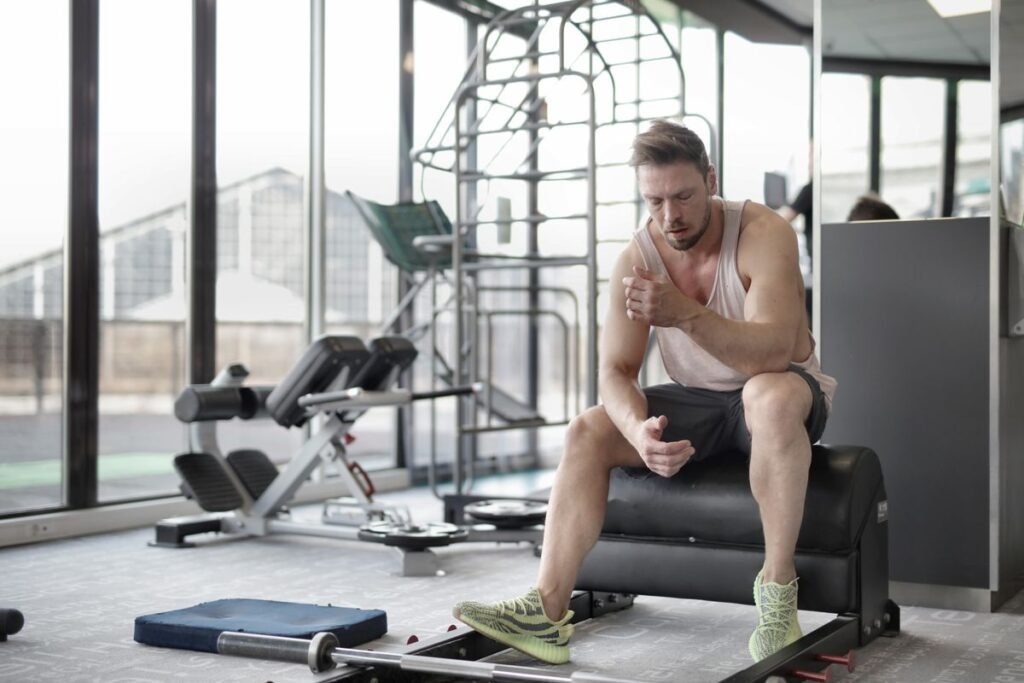 Hombre deportista descansando sentado en un banco entre series de entrenamiento en un gimnasio