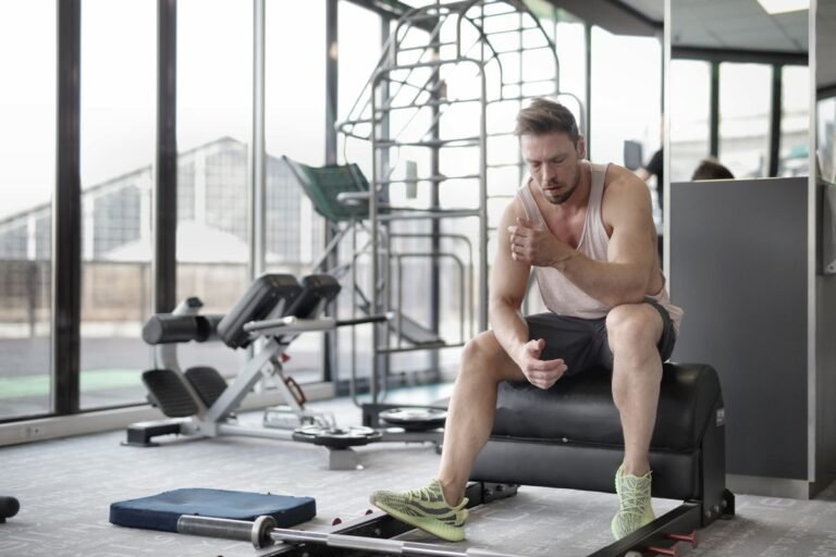 Hombre deportista descansando sentado en un banco entre series de entrenamiento en un gimnasio
